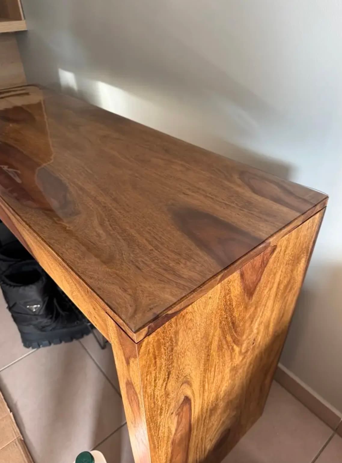 A narrow console made of dark, polished wood covered with soft glass, against a white wall