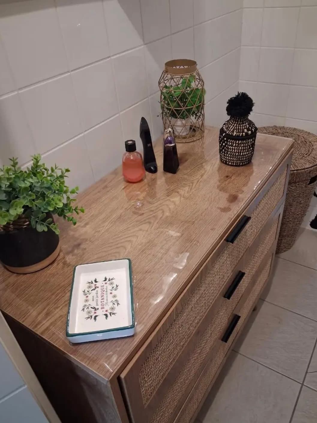 A chest of drawers made of wood and rattan - a mat on the top, soap, a lantern and a flower pot next to it
