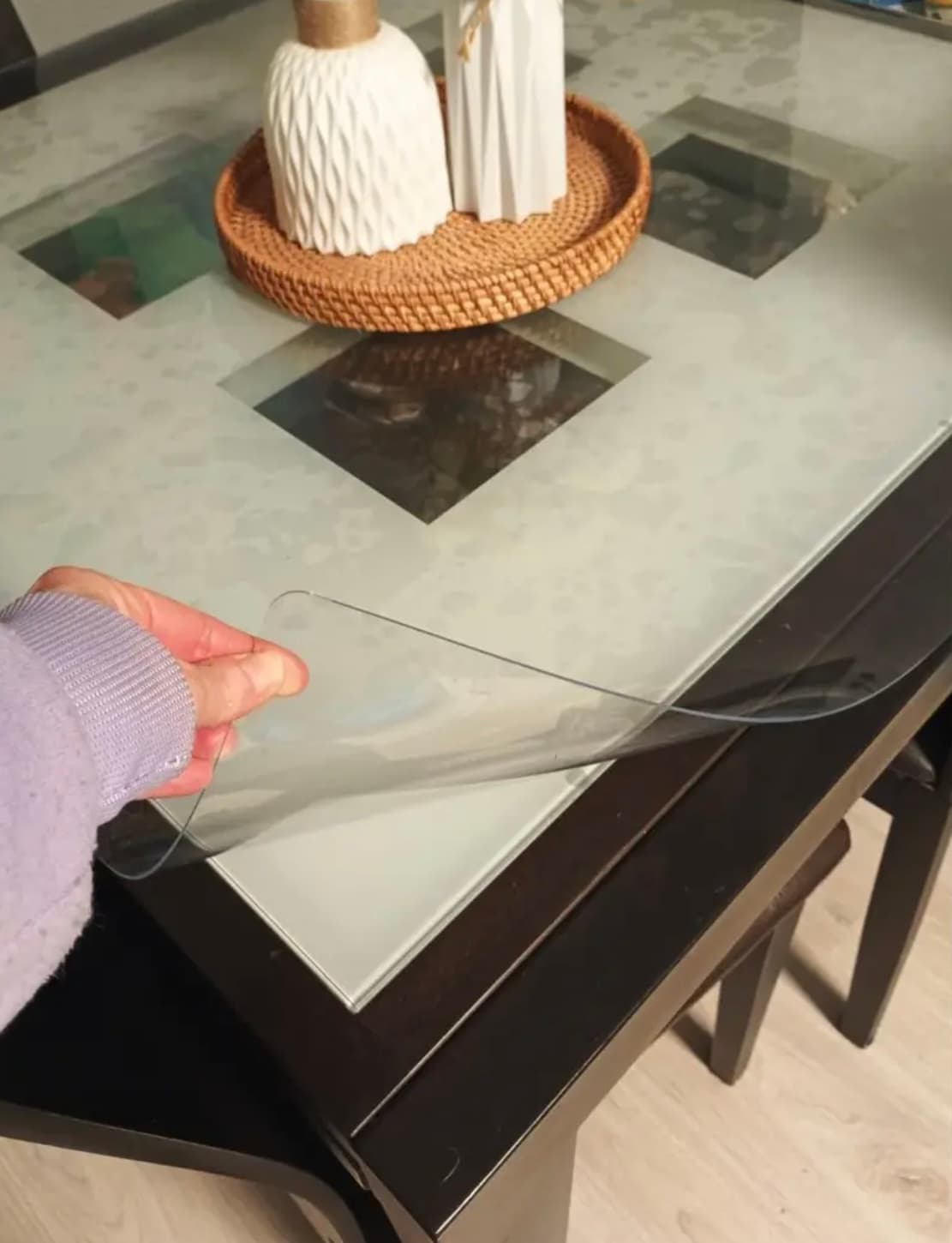 Hand tilts the corner of the mat from a dark table with a frosted glass top and a rattan tray in the center