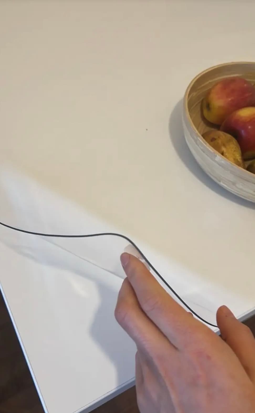 White countertop with a bowl of apples and pears; hand smoothes the edge of the clear overlay