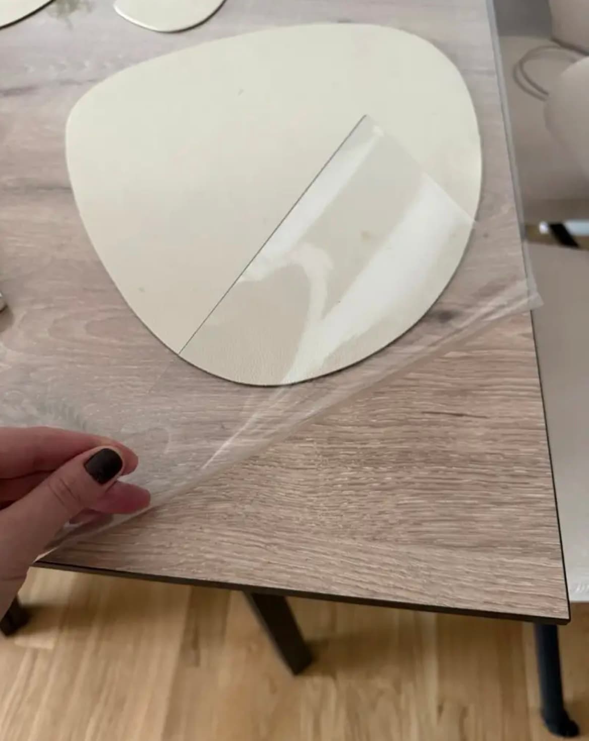 Fingers lift the thin mat over the cream placemat on the oak table - you can see how pliable it is