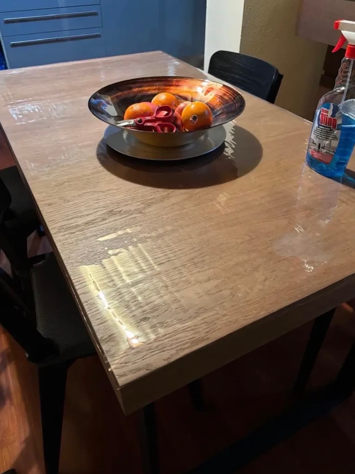 Metal bowl with oranges on an oak countertop; next to the mat there is a bottle of window cleaner