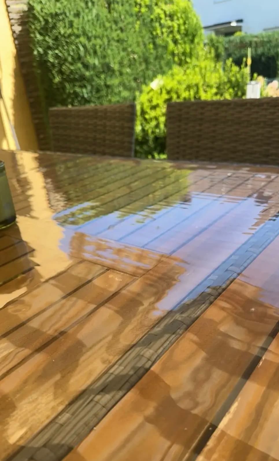 Garden table made of wooden slats; the hedge and sky are reflected in the mat