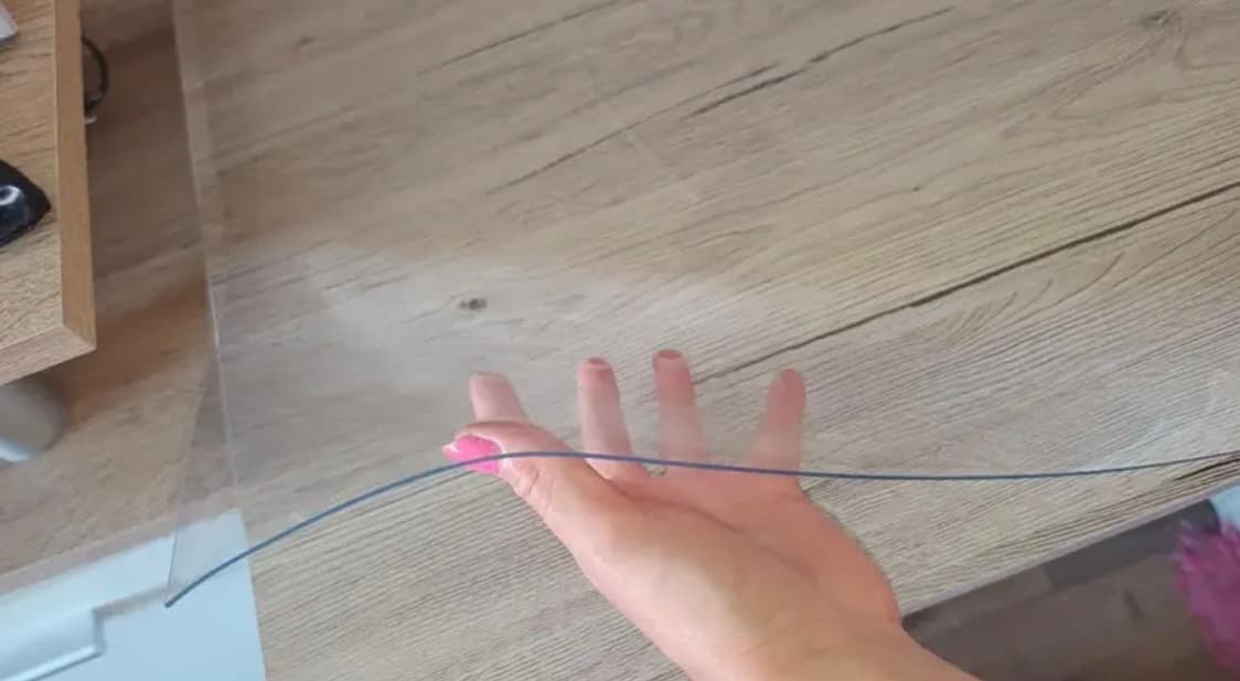 A hand slipped under a transparent mat lying on a light wooden countertop