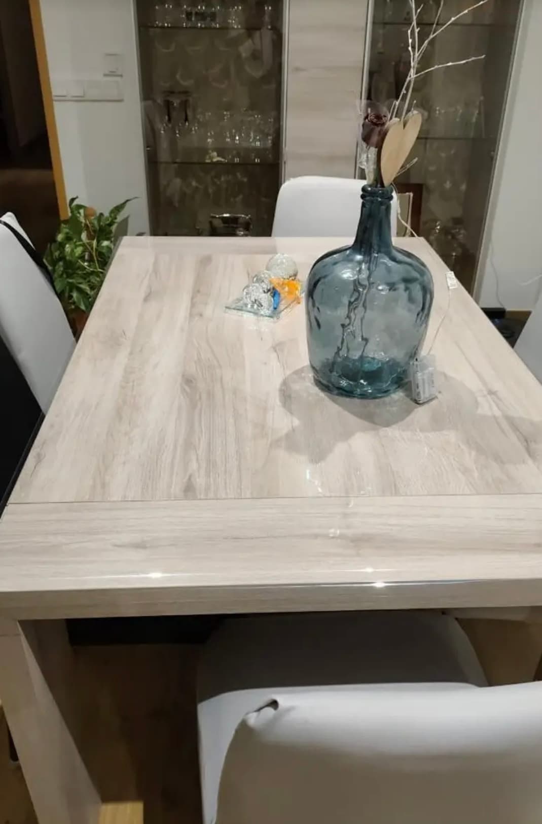 Extendable table in light wood with a large blue carboy; tabletop under soft glass