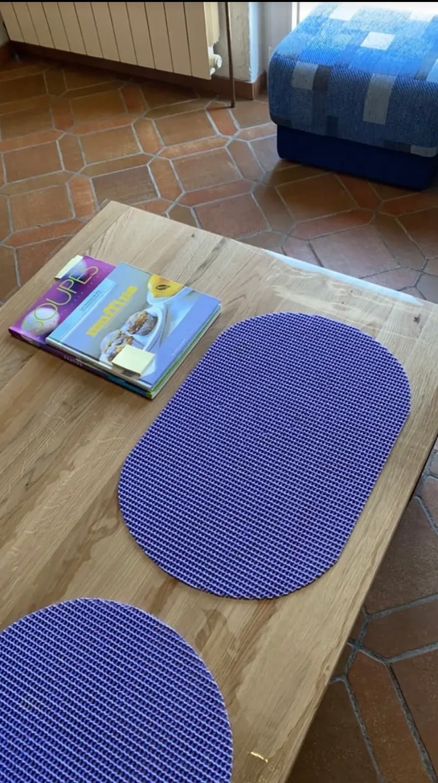 An oak table with purple placemats and cookbooks; the edge of the mat protrudes beyond the countertop