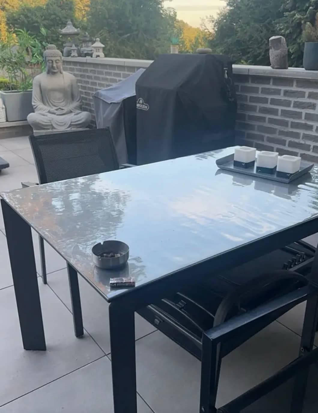Terrace with barbecue and stone statue; a table on a black frame covered with a transparent mat