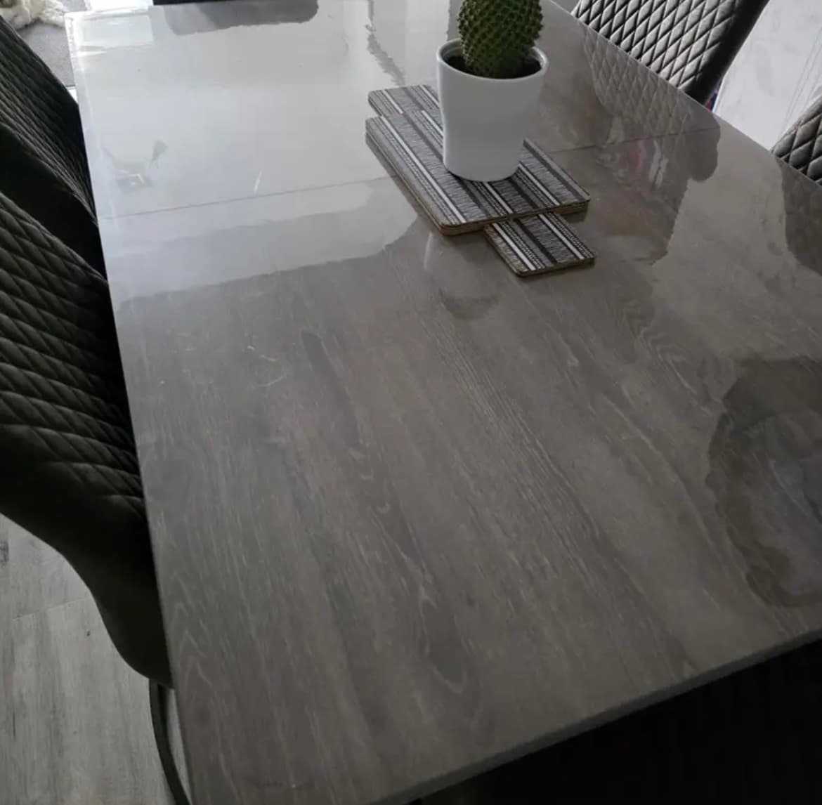 A gray stained table with a cactus on wooden placemats, quilted chairs around