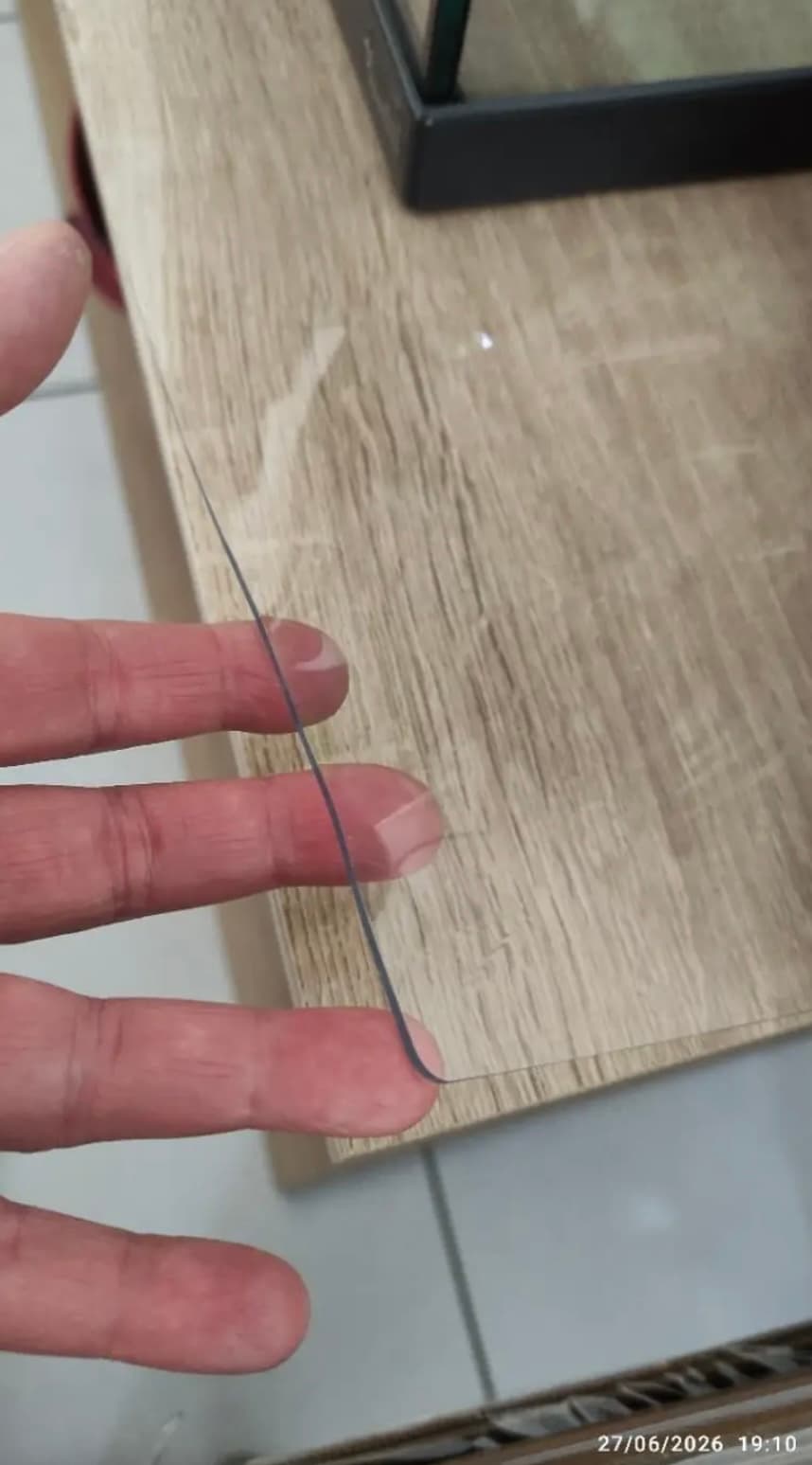 The fingers hold the corner of the mat on the oak countertop - when held up to the light you can see the thickness of the material