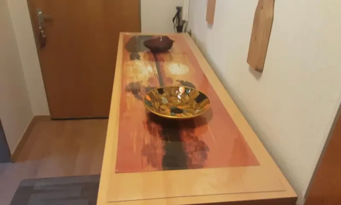 A narrow, bright table in the hall: a red tabletop pattern under the mat, a brass bowl on top
