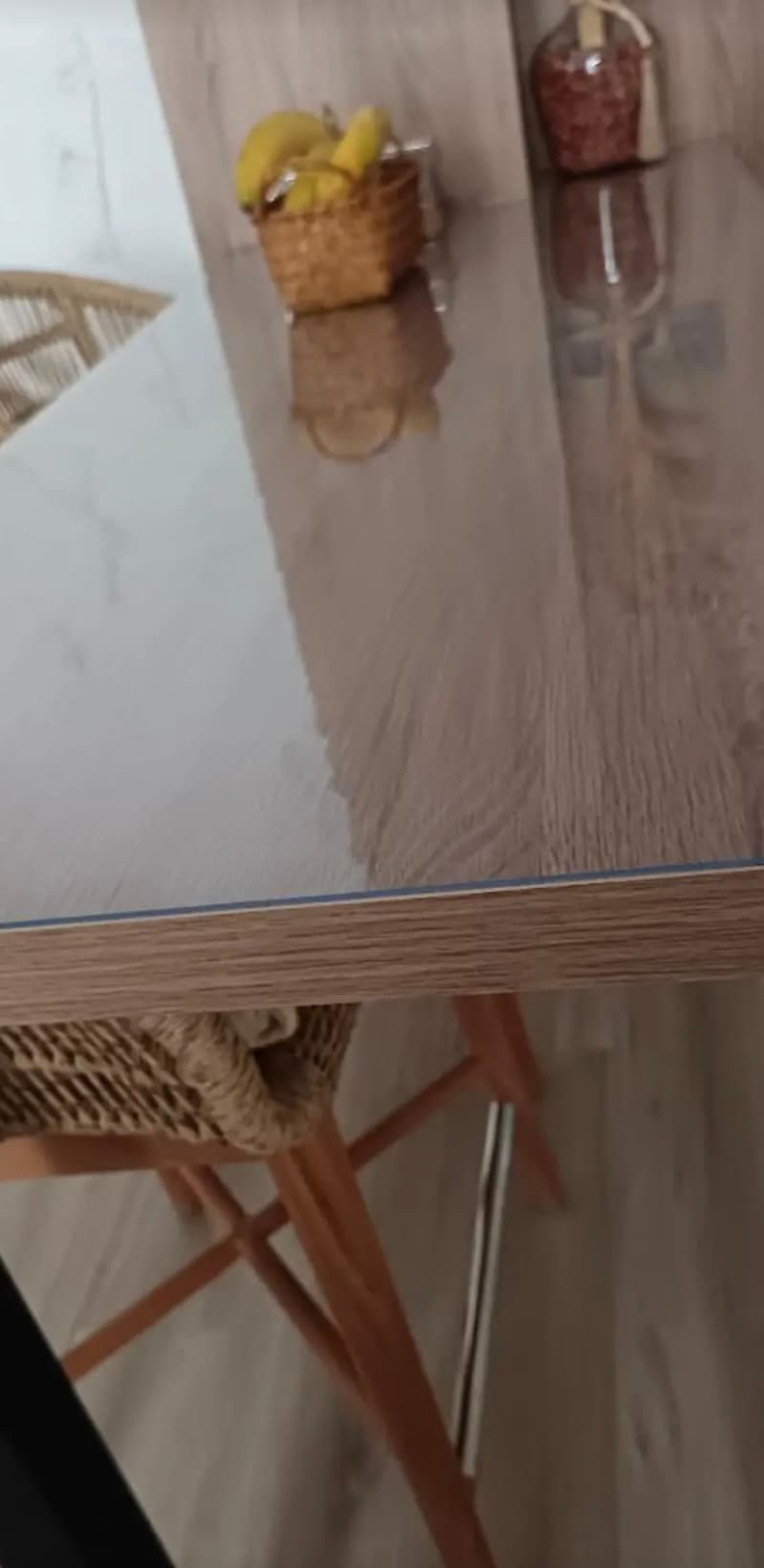 The corner of an oak table from above: a basket of bananas and a jar, a blue sheen can be seen in the edge of the mat
